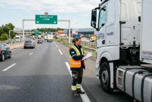 Agent de transport vérifiant un camion poids lourd sur autoroute, observé près d’un panneau Marseille–Lyon. Chauffeur poids lourd salaire évoqué.